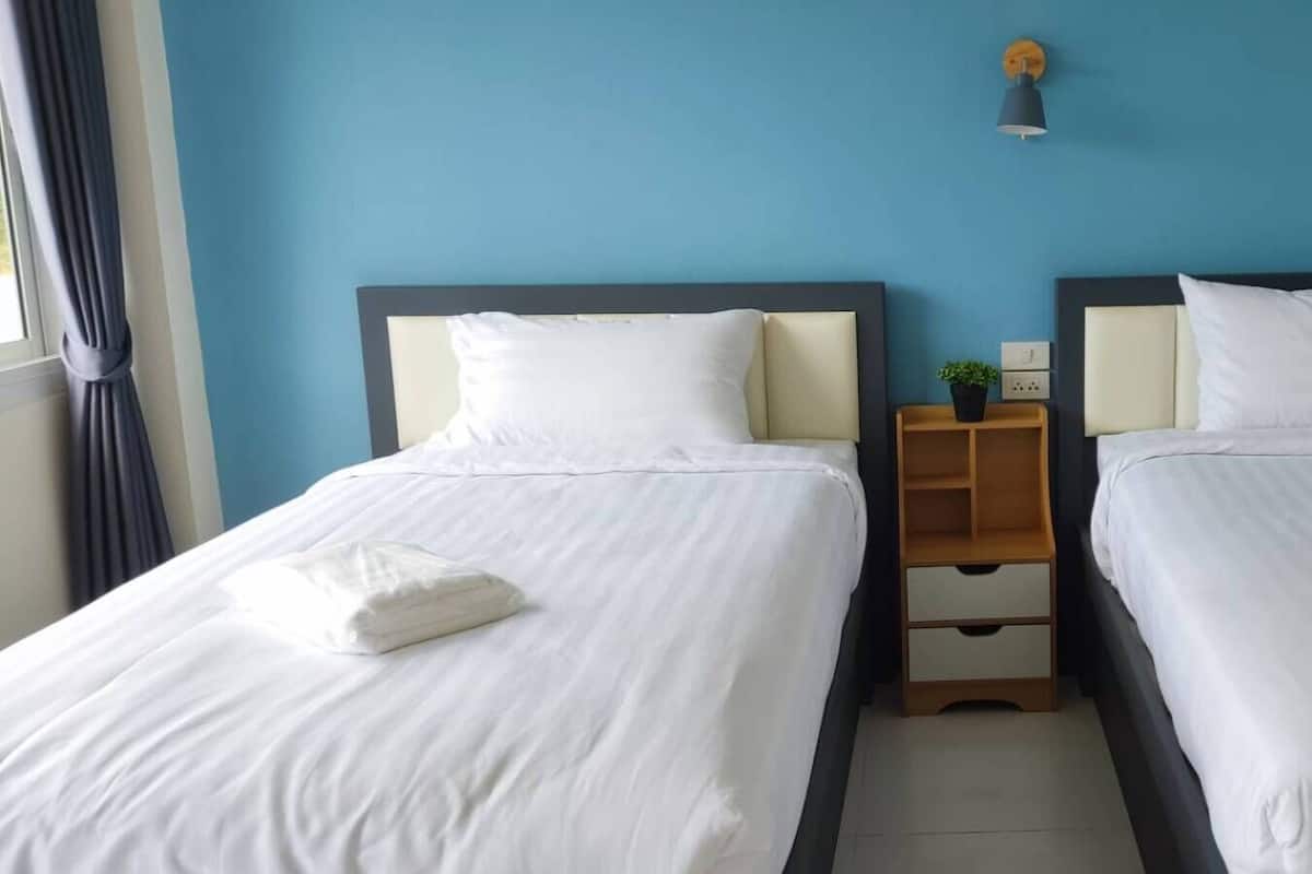Habitación de hotel con dos camas, cada una con sábanas y almohadas blancas, una mesita de noche de madera con cajones y una pequeña planta en maceta.