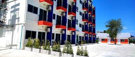 A multi-story hotel with balconies, air conditioning units, and a parking area.
