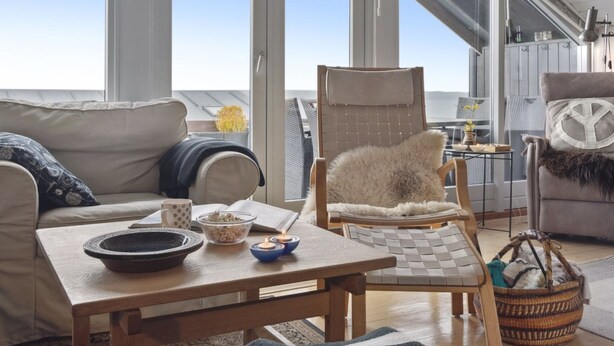 A cozy room with a sofa, a chair, a table, and a view of the sea through large windows.