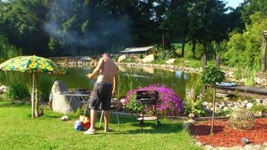 Una persona preparando comida a la parrilla al aire libre, con una parrilla, una mesa y una silla cerca.