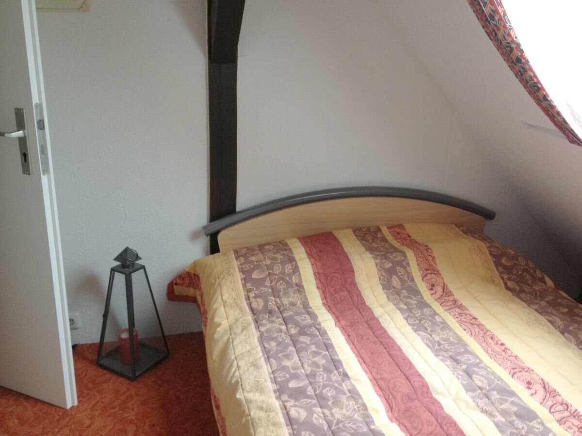 Un dormitorio con cama, una puerta y una mesita con una vela.