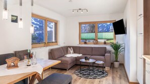 Ein modernes Wohnzimmer mit einer Couch, einem Esstisch und einem an der Wand befestigten Fernseher.