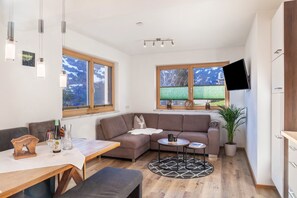 Una sala de estar moderna con un sofá, una mesa de comedor y un televisor montado en la pared.