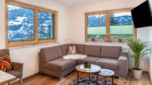 Ein modernes Wohnzimmer mit einer Eckcouch, einem runden Couchtisch und einem großen Fenster mit Blick auf die Berge.