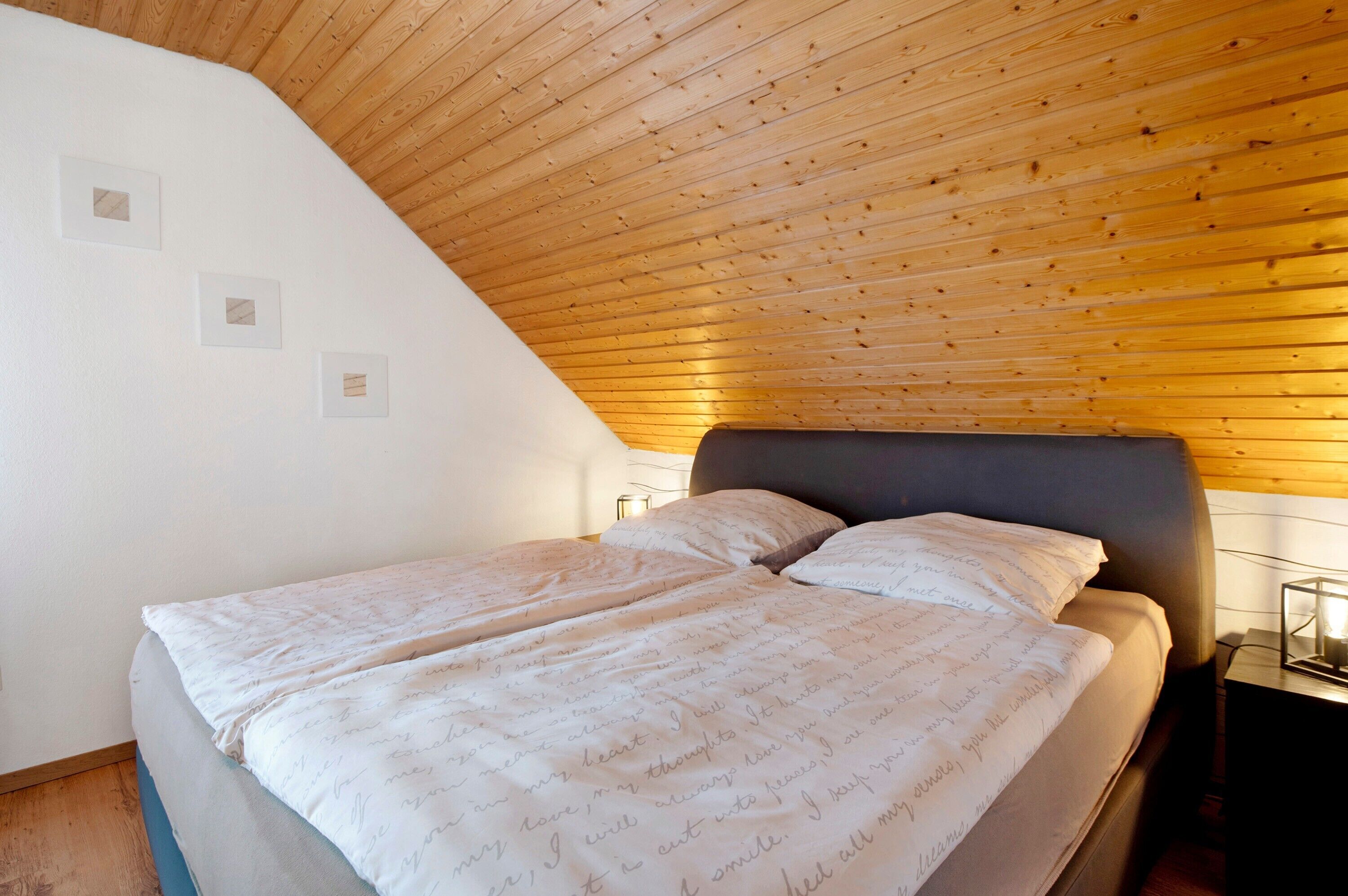 A bedroom with a sloped ceiling, a bed with a headboard, and bedside lamps.