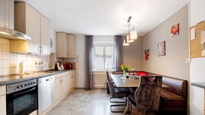 A modern kitchen with a dining area, featuring a built-in oven, a dining table with chairs, and a view through a window. - Holiday Apartment "Sink" with Private Terrace, Private Garden & Wi-Fi (Staufen)
