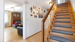 A staircase with wooden steps and blue carpet runners, a living room with a sofa and a cabinet, and a wall decorated with framed pictures and a deer painting. - Holiday Apartment "Sink" with Private Terrace, Private Garden & Wi-Fi (Staufen)