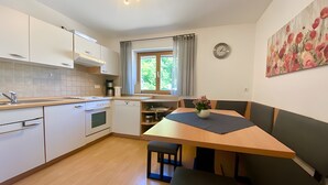 A modern kitchen with white cabinets, a wooden countertop, a dining table with benches, a clock on the wall, and a window with curtains. - Apartment 'Ferienwohnung 2' with Shared Garden, Balcony and Wi-Fi (Hagnau am Bodensee)