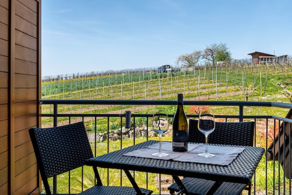 A balcony with a table, two chairs, a bottle of wine, and a glass on the table.