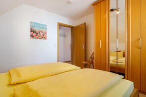 A bedroom with a bed, a wooden wardrobe, a door, and a painting on the wall.