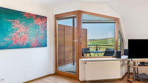 A room with a large window, a radiator, a TV, and a painting on the wall. - Apartment 'Ferienwohnung 2' with Shared Garden, Balcony and Wi-Fi (Hagnau am Bodensee)