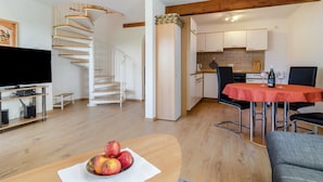 Ein modernes Wohnzimmer mit einer Holztreppe, einem Essbereich mit rotem Tisch und einer Küche im Hintergrund.
