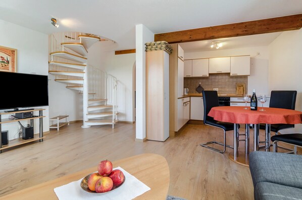 Una sala de estar moderna con una escalera de madera, un comedor con una mesa roja y una cocina al fondo.