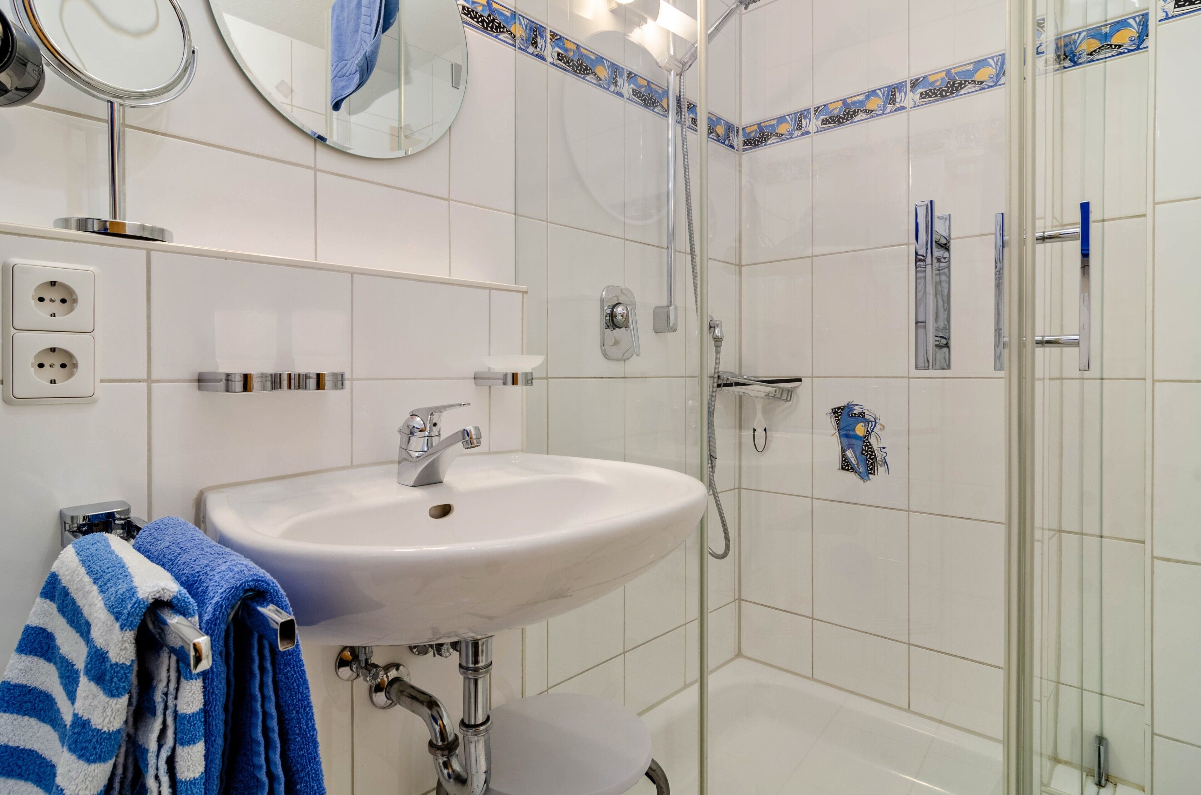 Ein Badezimmer mit Waschbecken, Spiegel, Dusche und Handtuchhalter.