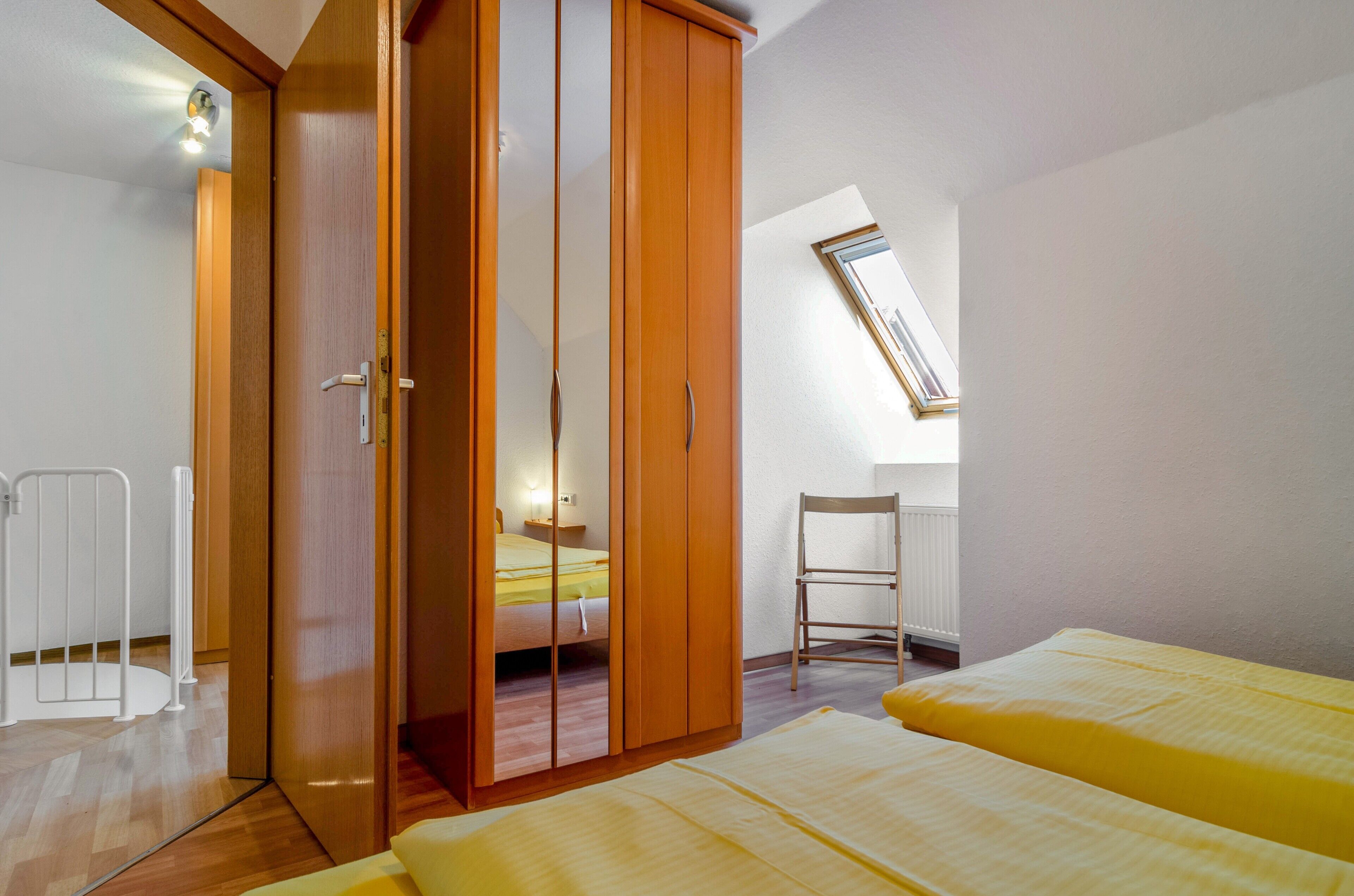 A bedroom with a bed, a wardrobe, a chair, and a skylight.