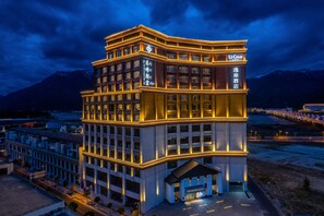 Un hotel de varios pisos con señalización iluminada, una entrada destacada y vistas a montañas al fondo.