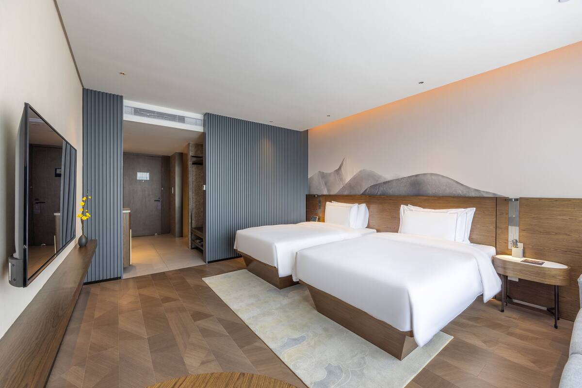 A hotel room with two beds, a large mirror, and a wall-mounted TV.