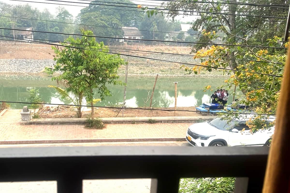 A view of a lake with a paved walkway, trees, and a parked car.