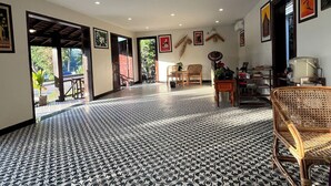 Een ruime kamer met patroon vloertegels, een rieten stoel en een eethoek met een tafel en stoelen.