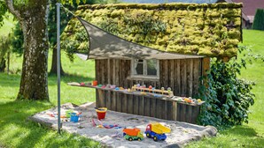 A wooden playhouse with a moss-covered roof, a small window, and a table with toys and a sandbox. - Holiday flat "DG", 85sqm, 2 bedrooms, max. 5 persons with panoramic view of nature (Nordrach)
