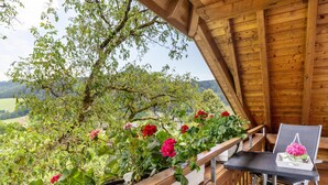 A wooden balcony with a table and chair, surrounded by greenery and flowers. - Holiday flat "DG", 85sqm, 2 bedrooms, max. 5 persons with panoramic view of nature (Nordrach)