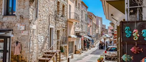 Una calle estrecha bordeada de edificios de piedra, algunos con balcones y carteles que indican negocios locales.