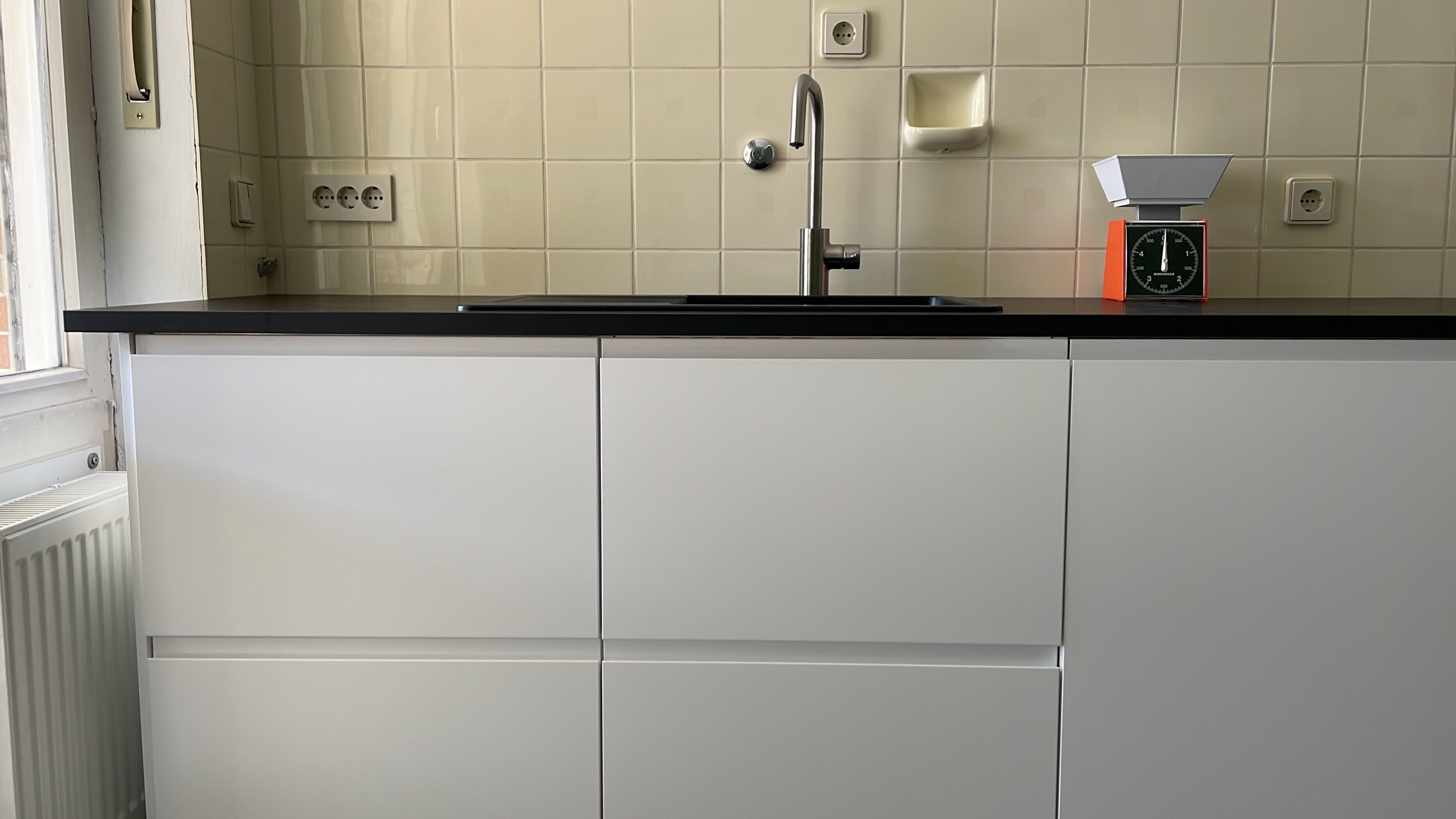 A kitchen with white cabinets, a black countertop, a faucet, and a coffee maker.