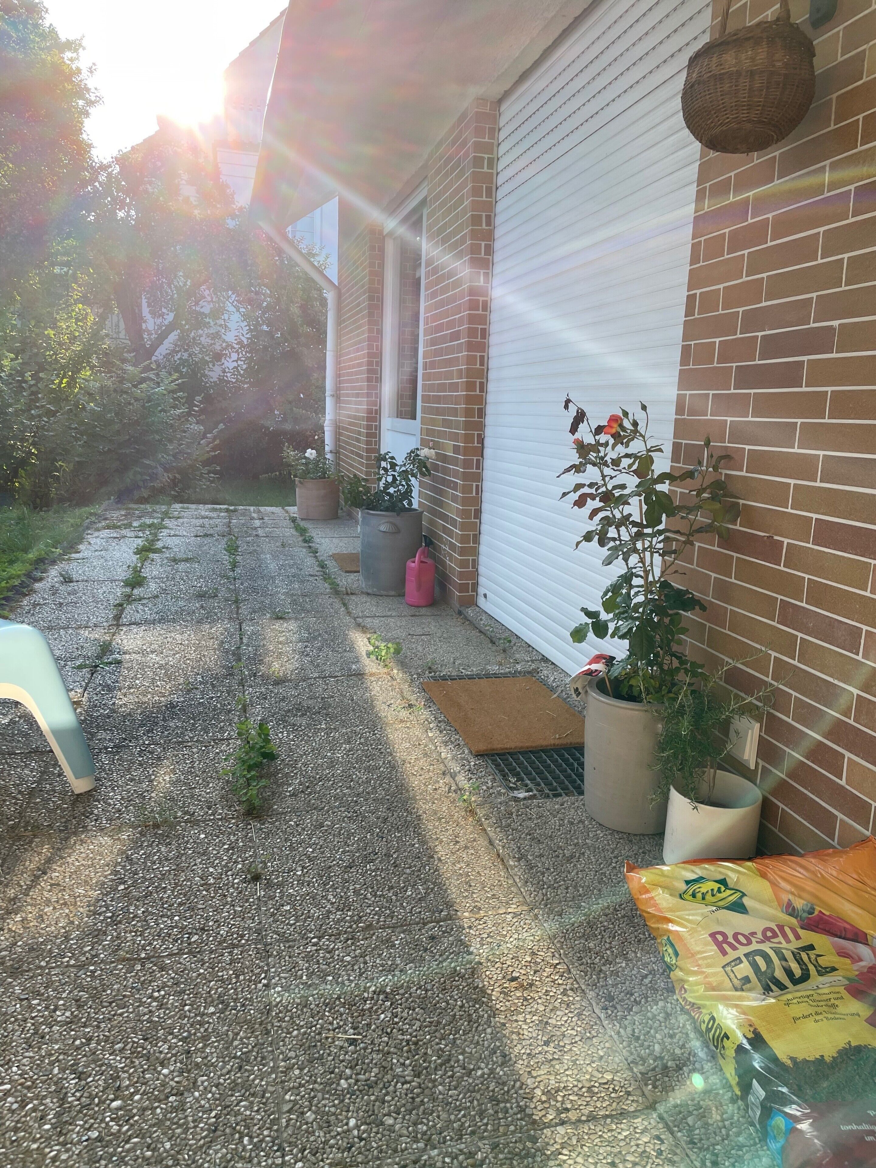 Een oprit met grind, planten in potten, een deur en een garage.