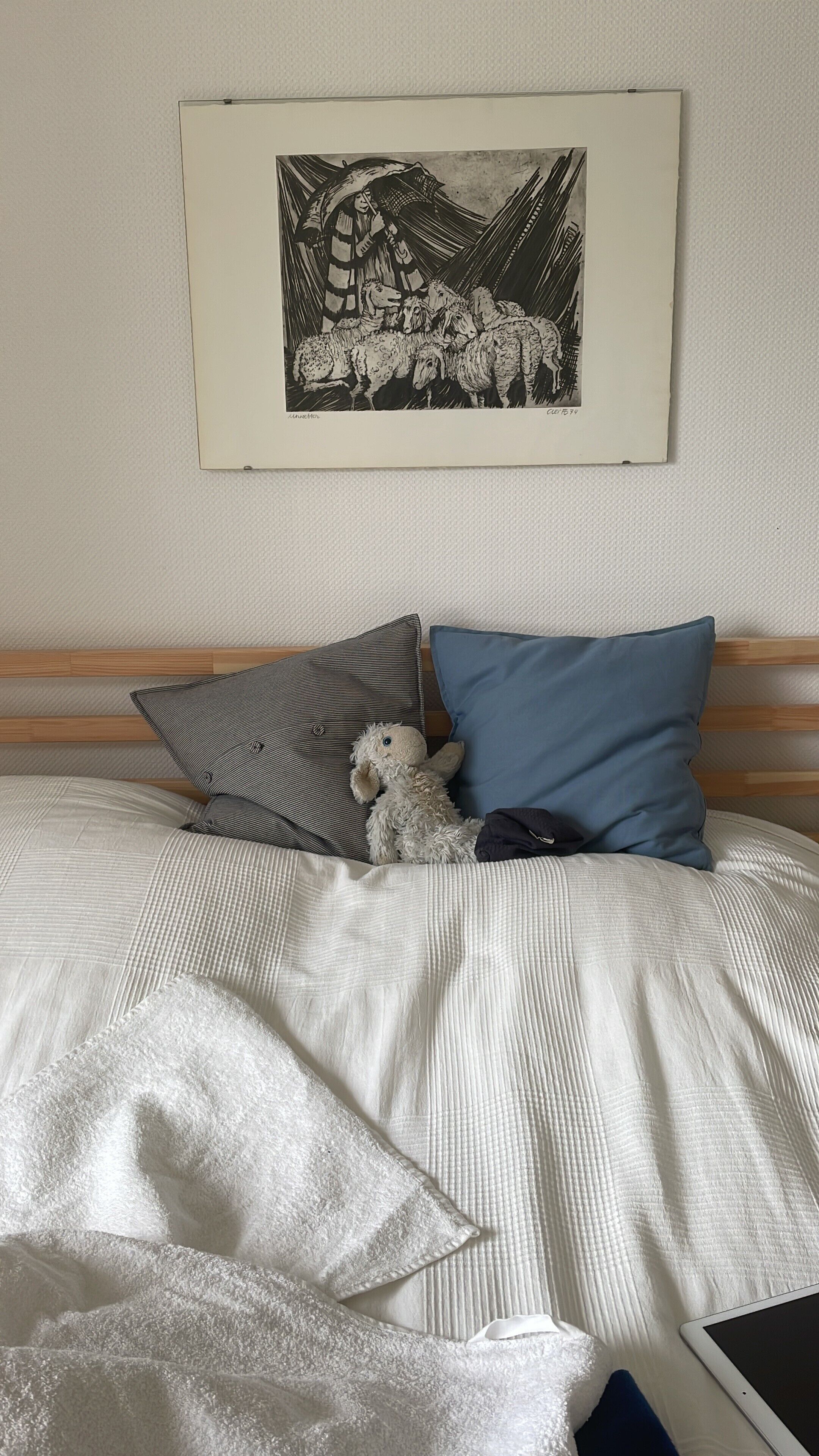 Un lit avec un oreiller à rayures, un oreiller bleu et un jouet en peluche. Un tableau encadré est accroché au mur au-dessus du lit.