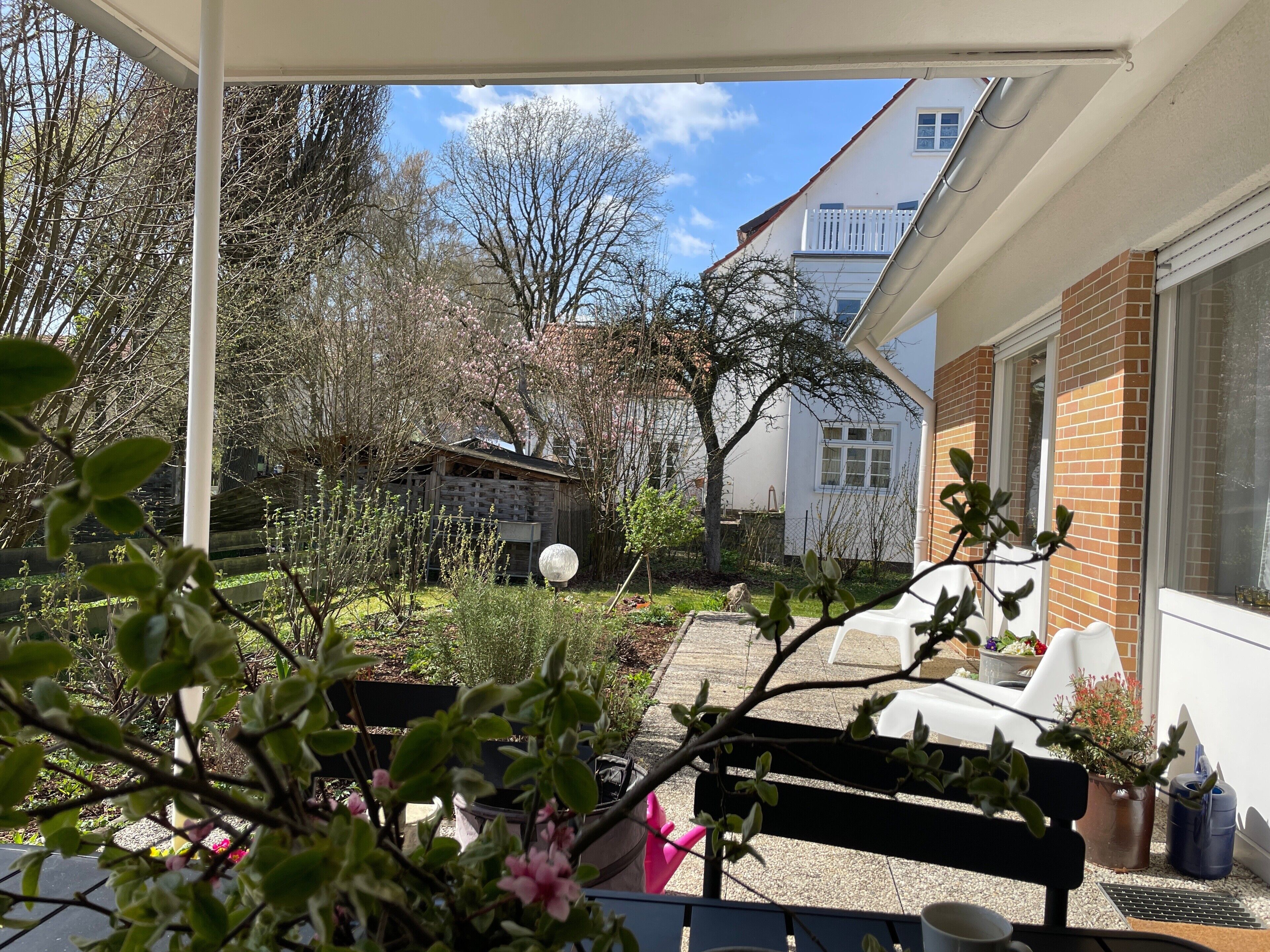 Ein überdachter Außenbereich mit einer Bank, Topfpflanzen und einem kleinen Garten.