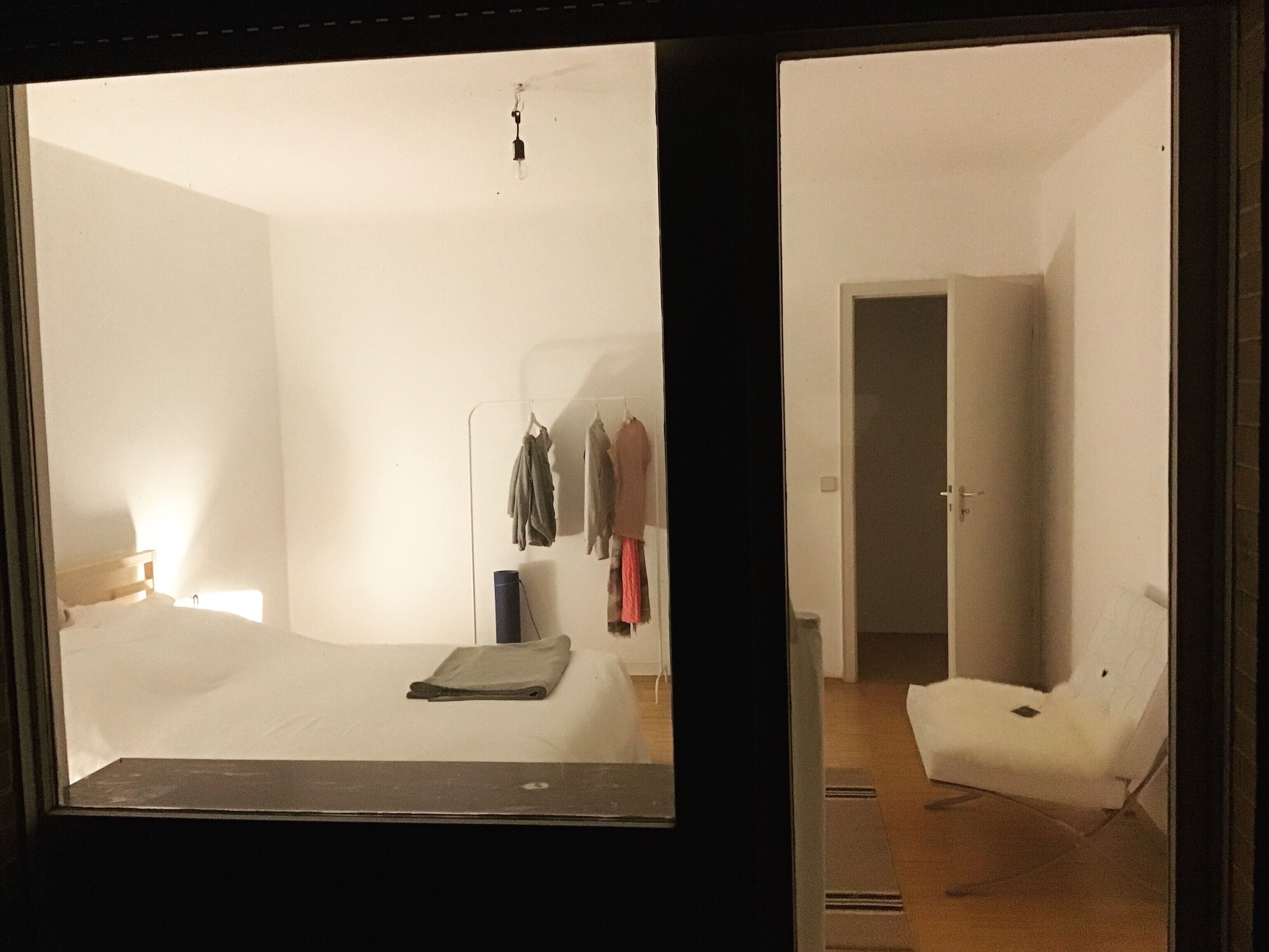 Une chambre à coucher comprenant un lit, une table de chevet, un portant à vêtements et une porte donnant sur une autre pièce.