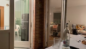 Uma cozinha com geladeira, porta de vidro que dá para uma sala de jantar e uma mesa com garrafa e copos.