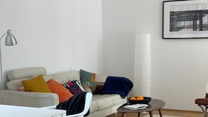 Uma sala de estar moderna com um sofá branco, uma mesa de centro, uma mesa de jantar e uma cadeira.