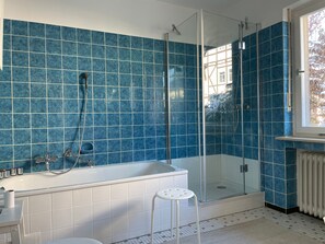 A modern bathroom with a glass-enclosed shower, a white bathtub, and a small stool.