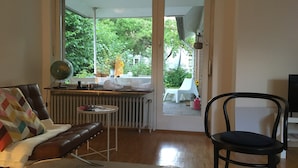 Um quarto com um sofá de couro marrom, uma cadeira preta, uma mesinha redonda e um radiador.