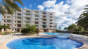 Ein modernes Hotel mit Poolbereich, das einen gewölbten Pool, Palmen und ein mehrstöckiges Gebäude mit Balkonen zeigt.