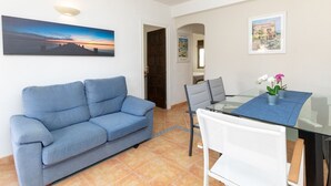 Ein Wohnzimmer mit einem blauen Sofa, einem Glastisch mit Stühlen und Blick ins Freie.
