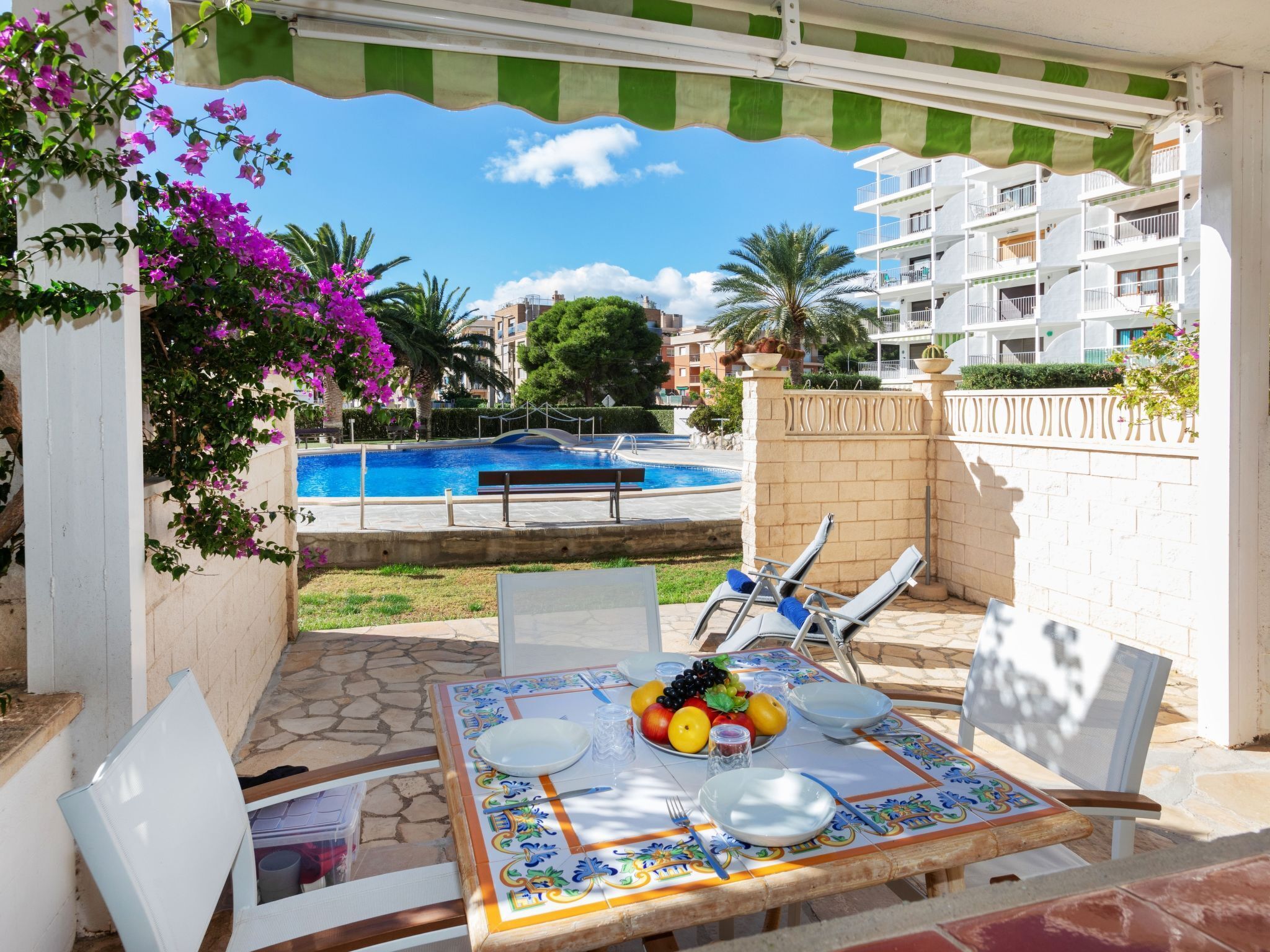A poolside patio with a table set for dining, a pool, and a view of a residential building.