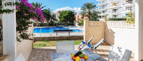 A poolside patio with a table set for dining, a pool, and a view of a residential building.