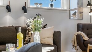 A modern living room with a sofa, armchair, and a small table with a vase of flowers and a bottle.
