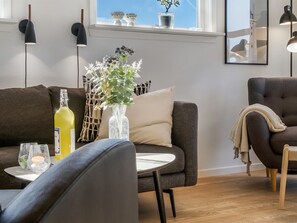 A modern living room with a sofa, armchair, and a small table with a vase of flowers and a bottle.