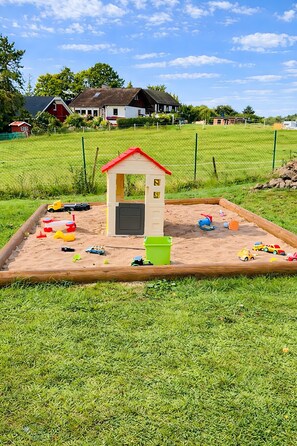A sandbox with a small playhouse and various toys.