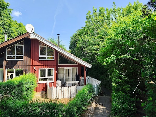 A red wooden house with a satellite dish, a white picket fence, and a pathway leading to the house.
