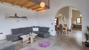 A modern living room with a grey sofa, a glass coffee table, and a purple rug. There is a dining area with a wooden table and chairs, and a kitchen visible through an archway.