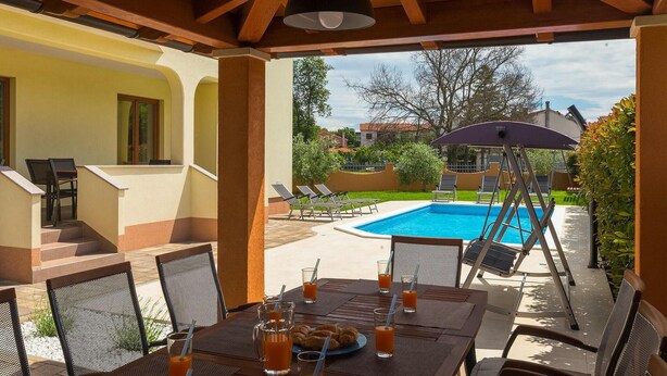 An outdoor patio with a pool, lounge chairs, and a table set for dining.