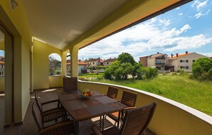 Un balcon avec une table dressée pour le dîner, donnant sur un quartier résidentiel avec des maisons et de la verdure.
