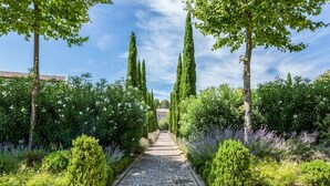 A stone pathway flanked by neatly trimmed hedges and tall cypress trees, leading towards a building with a red-tiled roof. - Lovely home in Saint-Laurent-de-la-Ca with WiFi (Saint-Laurent-de-la-Ca)