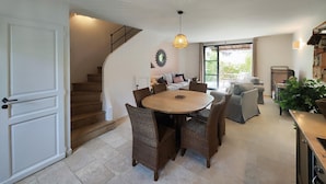 A spacious dining area with a round wooden table surrounded by wicker chairs, a staircase leading to another level, and a view of the outdoors through a large window. - Lovely home in Saint-Laurent-de-la-Ca with WiFi (Saint-Laurent-de-la-Ca)