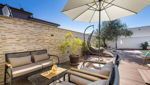 Une terrasse avec un canapé, des chaises, une table et un fauteuil suspendu.