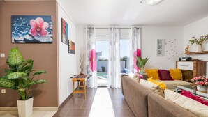 Un salon avec un canapé, une table basse et un baby-foot. Il y a une grande fenêtre avec des rideaux, une plante et un tableau au mur.